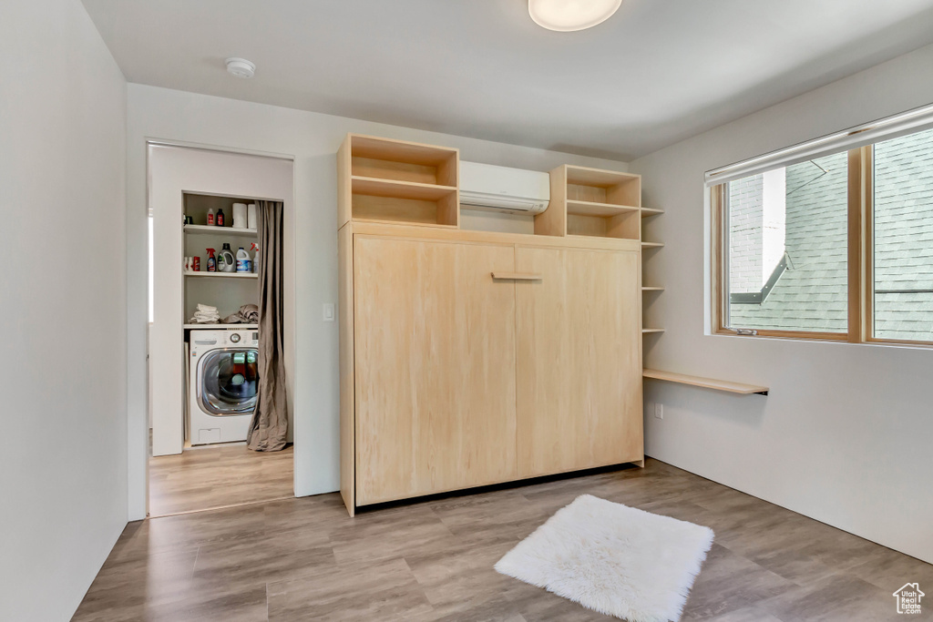 Bedroom with washer / clothes dryer, light wood-type flooring, and an AC wall unit