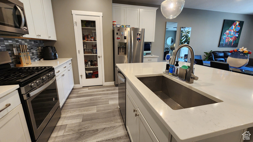 Kitchen with a kitchen island with sink, light hardwood / wood-style flooring, backsplash, stainless steel appliances, and sink