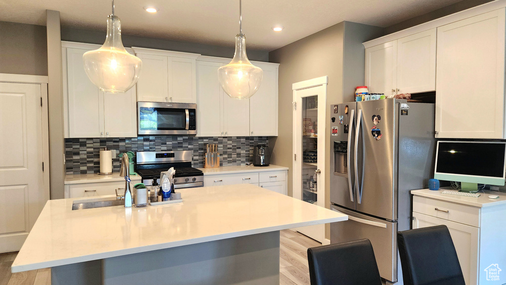 Kitchen featuring pendant lighting, white cabinetry, light hardwood / wood-style flooring, an island with sink, and appliances with stainless steel finishes