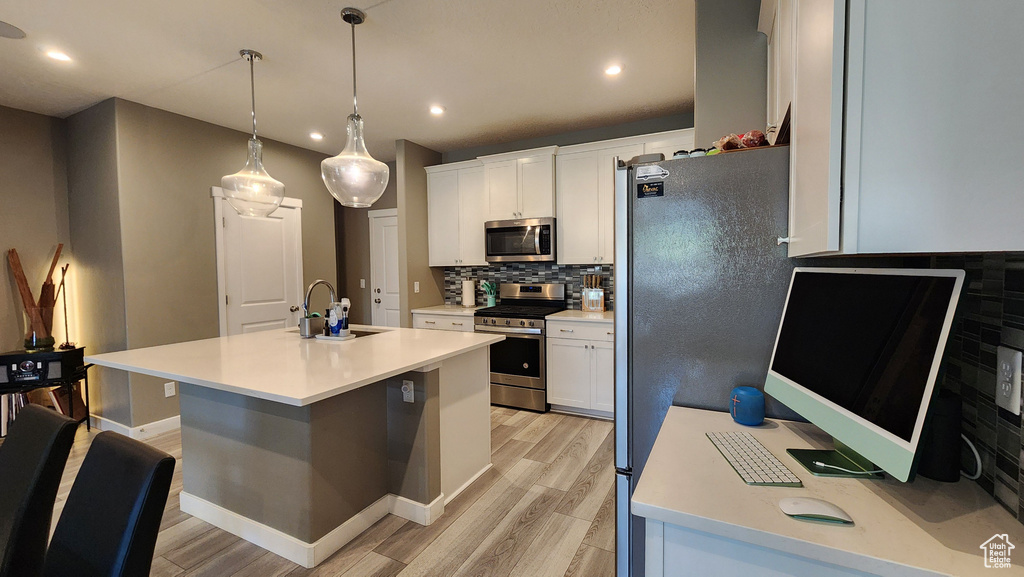 Kitchen with white cabinets, light hardwood / wood-style flooring, stainless steel appliances, sink, and a center island with sink