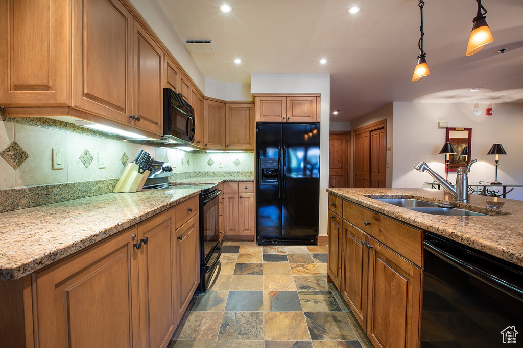 Kitchen with decorative light fixtures, light stone countertops, sink, black appliances, and tasteful backsplash