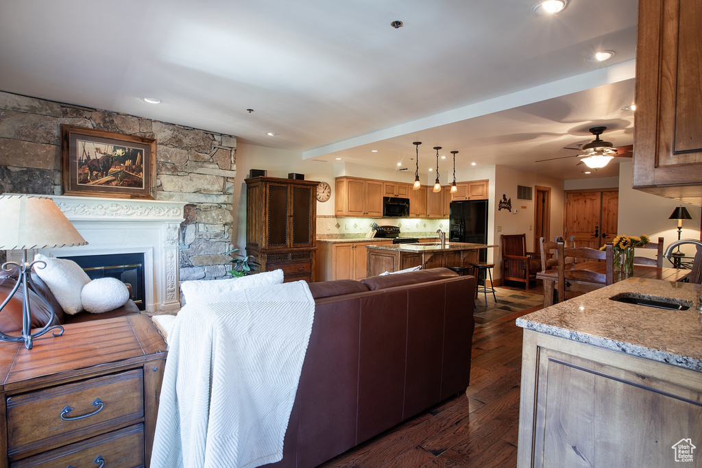 Living room featuring sink, ceiling fan, dark hardwood / wood-style flooring, and a stone fireplace