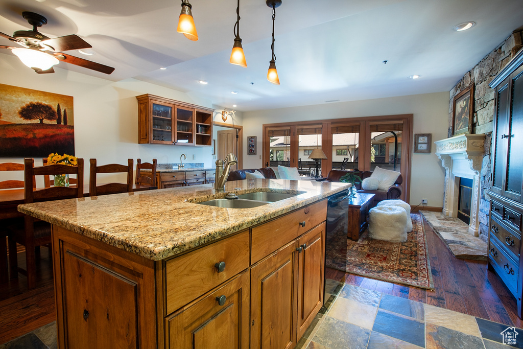 Kitchen with a kitchen island with sink, sink, ceiling fan, dark hardwood / wood-style floors, and a stone fireplace