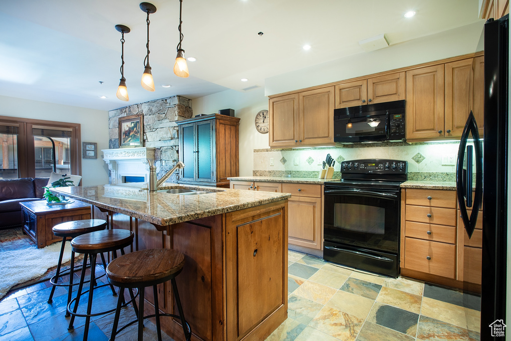 Kitchen featuring decorative light fixtures, black appliances, light stone counters, sink, and a center island with sink