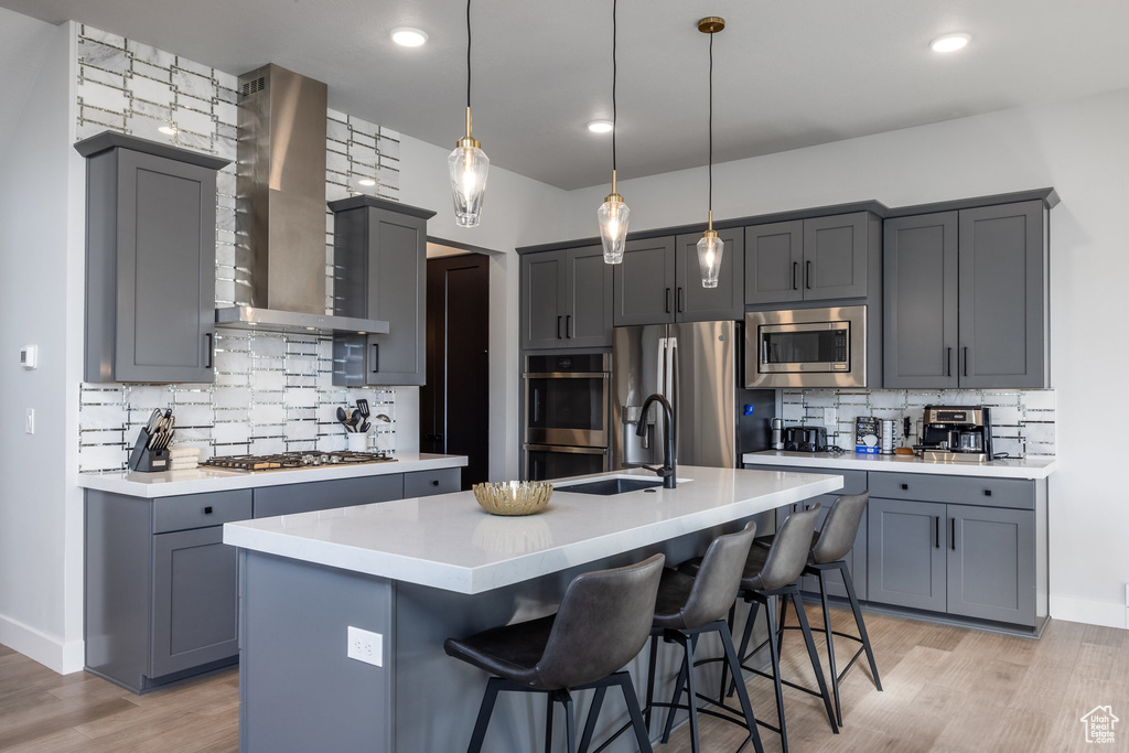 Kitchen featuring gray cabinets, tasteful backsplash, stainless steel appliances, and a kitchen island with sink