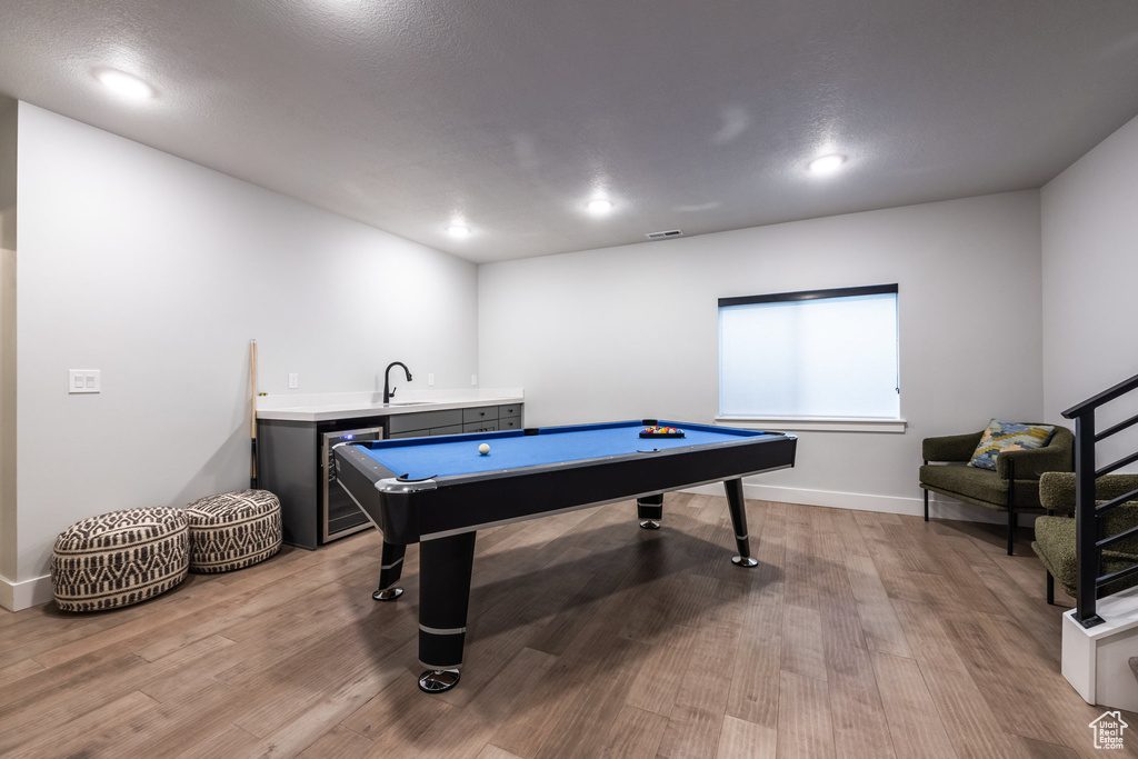 Game room with wet bar, a textured ceiling, and light hardwood / wood-style flooring