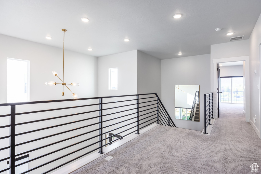 Hallway featuring light colored carpet and a notable chandelier