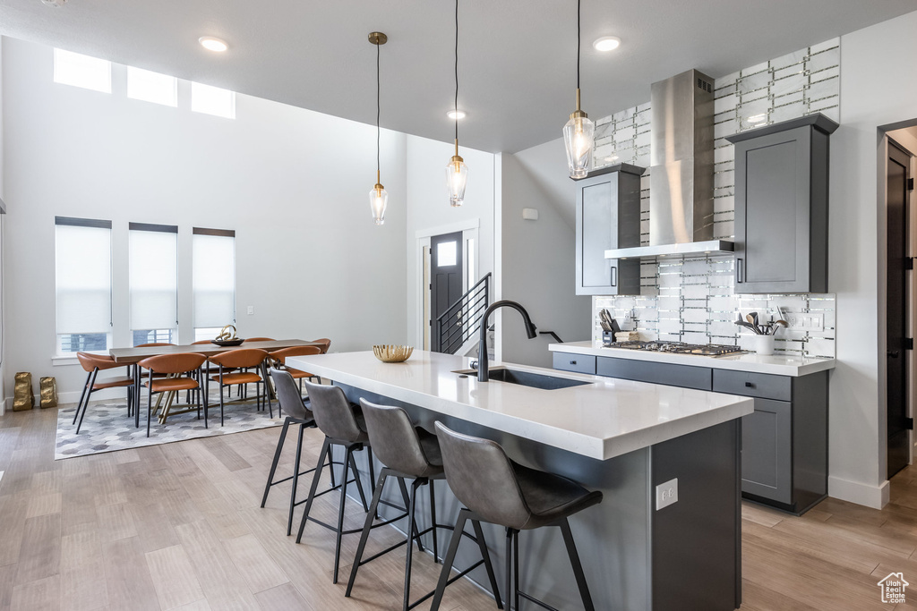 Kitchen featuring wall chimney exhaust hood, pendant lighting, light hardwood / wood-style flooring, sink, and gray cabinets