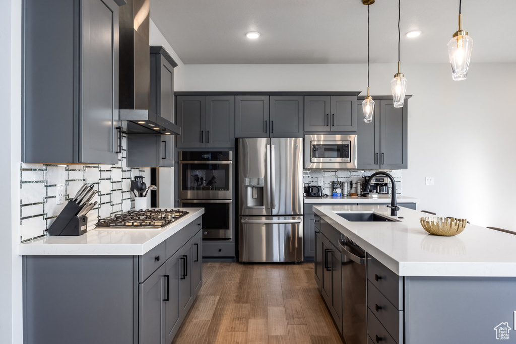 Kitchen with pendant lighting, sink, dark wood-type flooring, wall chimney exhaust hood, and appliances with stainless steel finishes