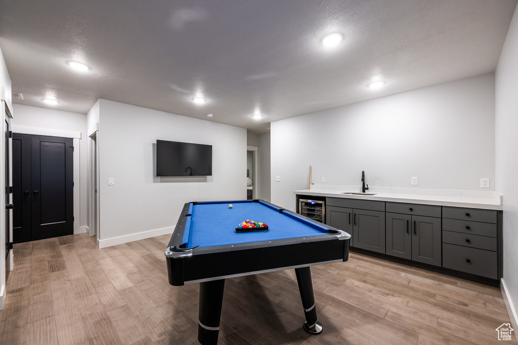 Recreation room featuring pool table, light hardwood / wood-style floors, beverage cooler, indoor wet bar, and a textured ceiling