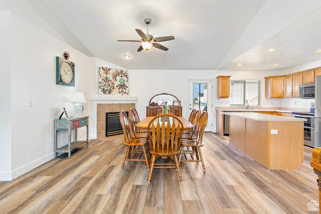 Dining space featuring ceiling fan, light wood-type flooring, vaulted ceiling, and a fireplace