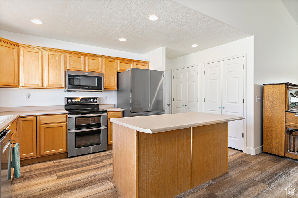 Kitchen with appliances with stainless steel finishes, a kitchen island, wood-type flooring, and a textured ceiling