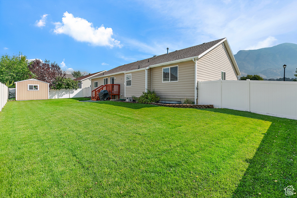 Rear view of house featuring a mountain view, a lawn, and a storage unit