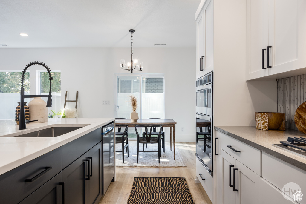 Kitchen featuring light hardwood / wood-style floors, sink, stainless steel appliances, hanging light fixtures, and white cabinets