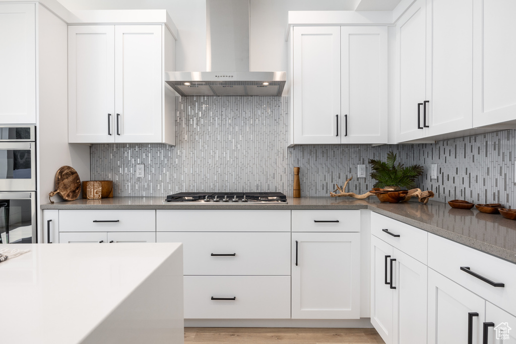 Kitchen featuring wall chimney range hood, white cabinets, stainless steel appliances, and light wood-type flooring