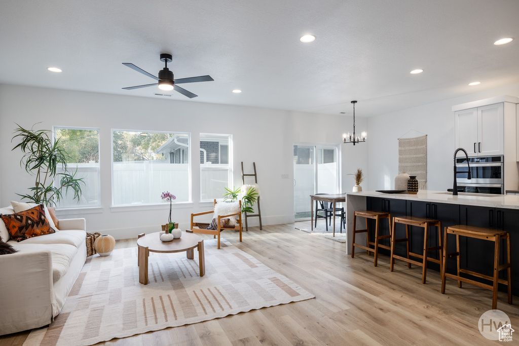 Living room featuring ceiling fan with notable chandelier and light wood-type flooring