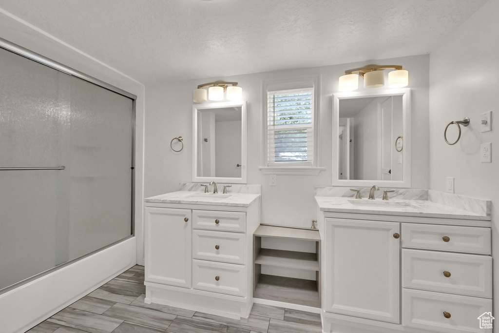 Bathroom with enclosed tub / shower combo, wood-type flooring, a textured ceiling, and vanity