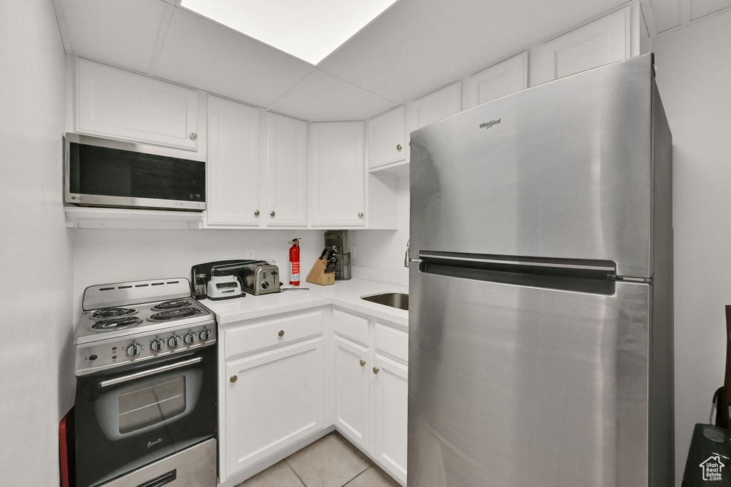 Kitchen with white cabinets, light tile patterned floors, and stainless steel appliances