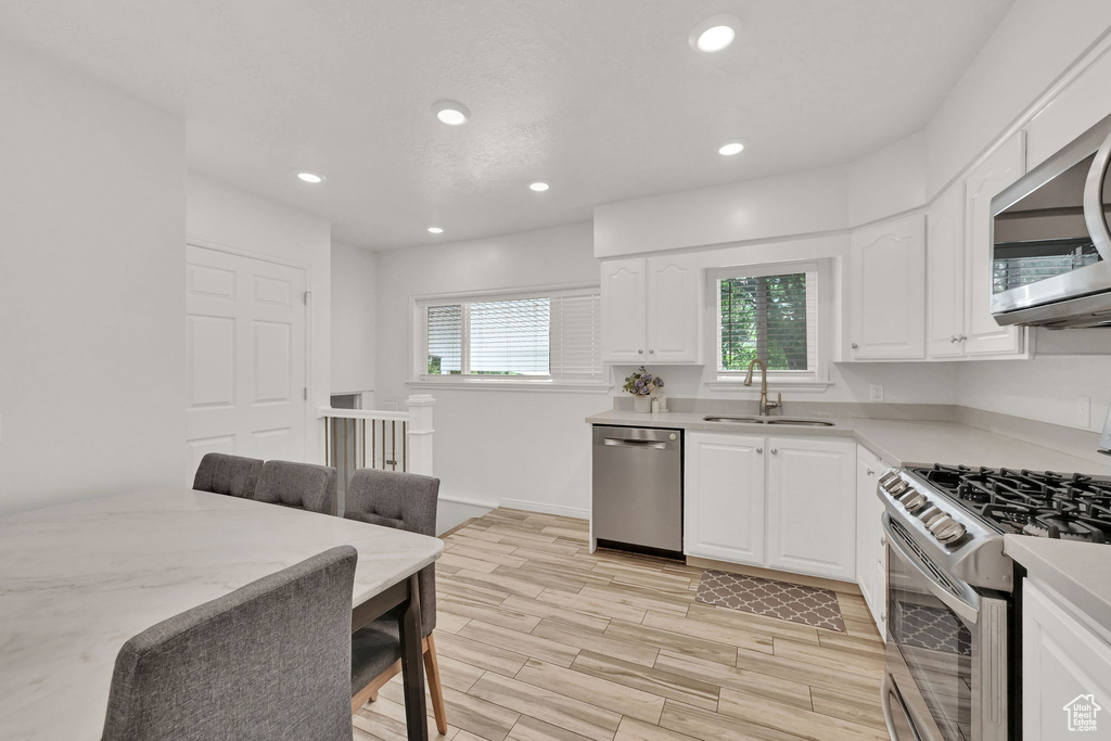 Kitchen with white cabinets, appliances with stainless steel finishes, light hardwood / wood-style floors, and sink