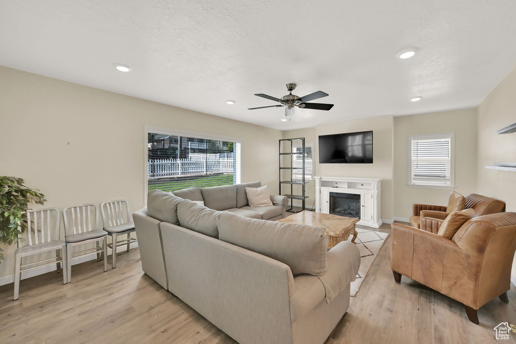 Living room with light wood-type flooring, ceiling fan, a wealth of natural light, and a textured ceiling