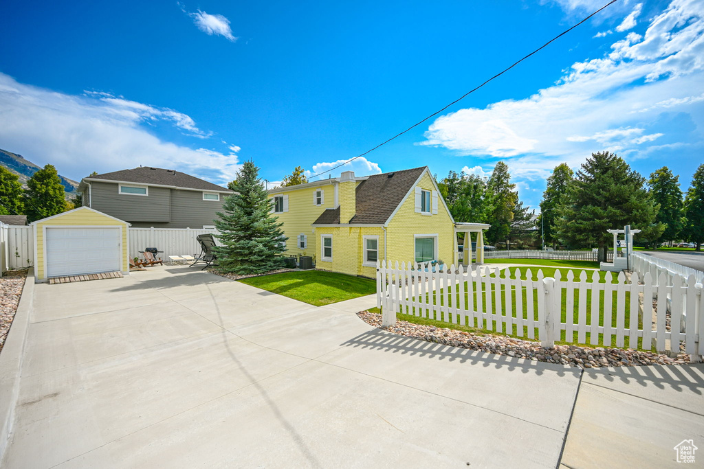 View of front of house with cooling unit, a garage, an outbuilding, and a front yard