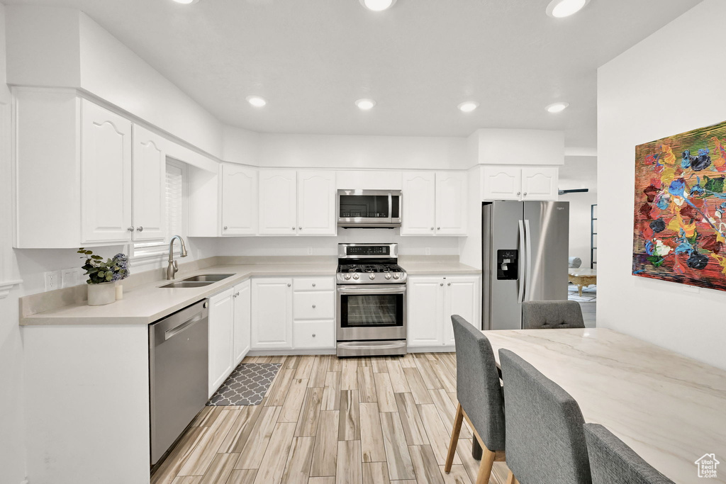 Kitchen with light hardwood / wood-style flooring, sink, appliances with stainless steel finishes, and white cabinets