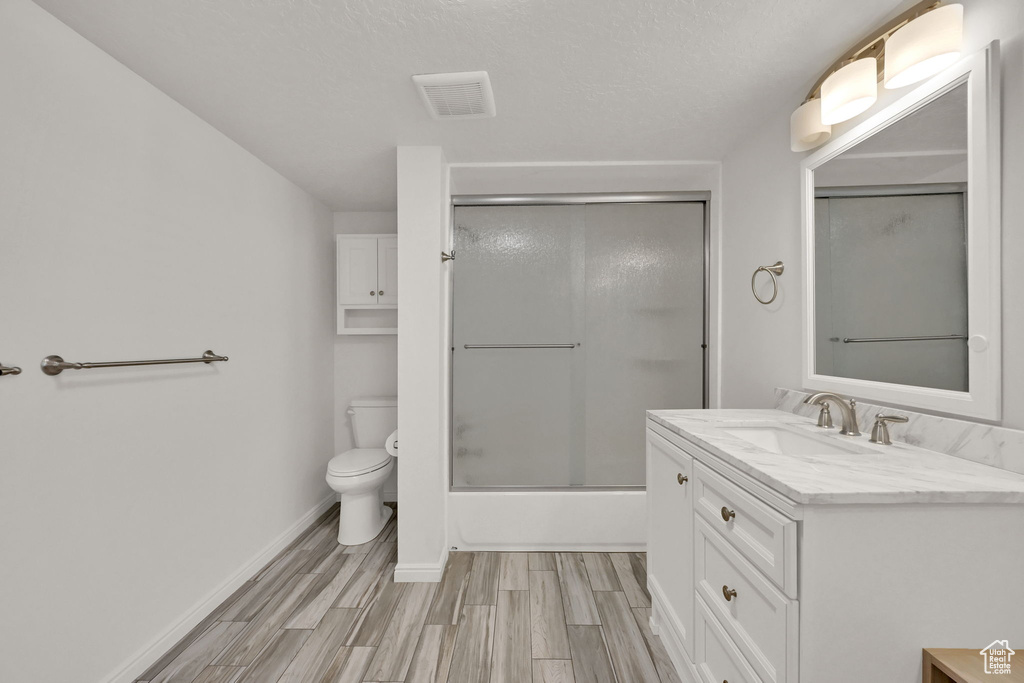 Full bathroom featuring toilet, vanity, a textured ceiling, wood-type flooring, and enclosed tub / shower combo