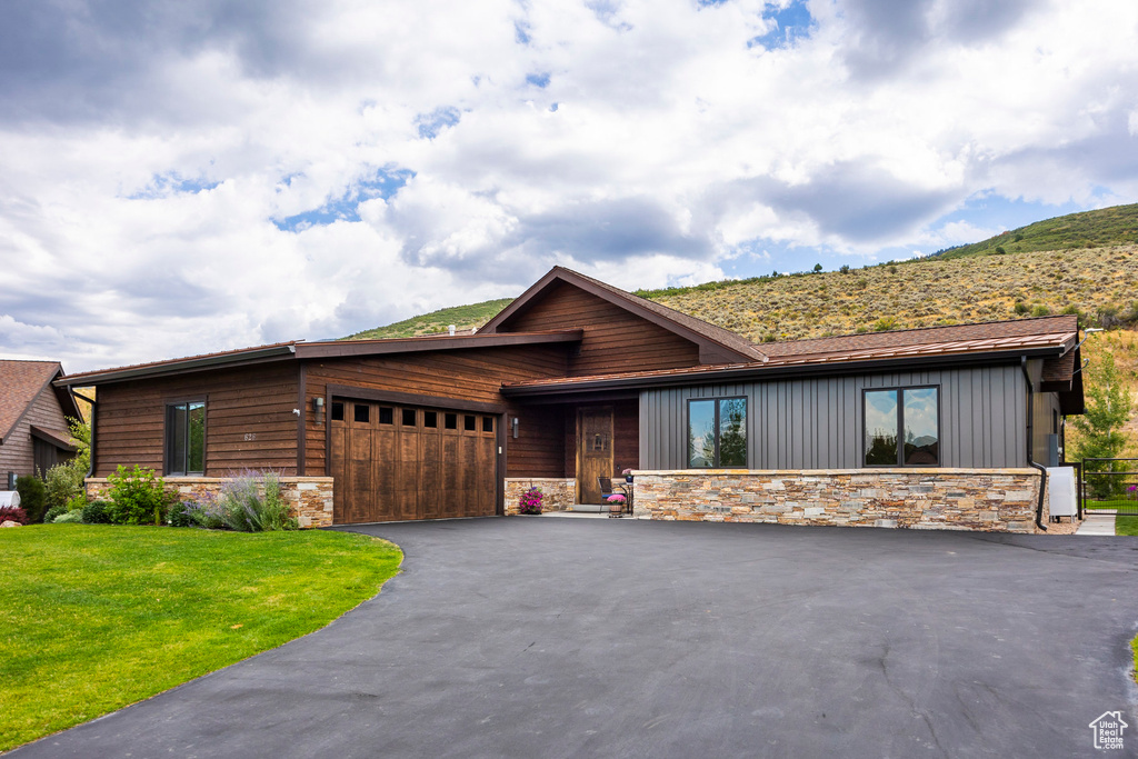 View of front of house featuring stone siding, an attached garage, driveway, and a front lawn