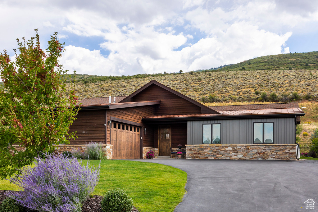 View of front of property featuring stone siding, a standing seam roof, an attached garage, metal roof, and driveway