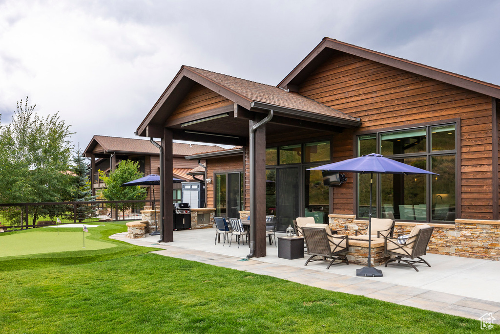 Back of property with an area to practice putting, a patio area, a yard, and a fire pit