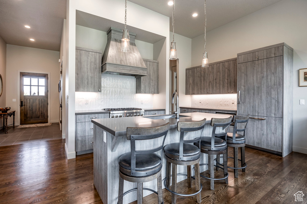Kitchen with a breakfast bar, modern cabinets, a sink, a center island with sink, and custom range hood
