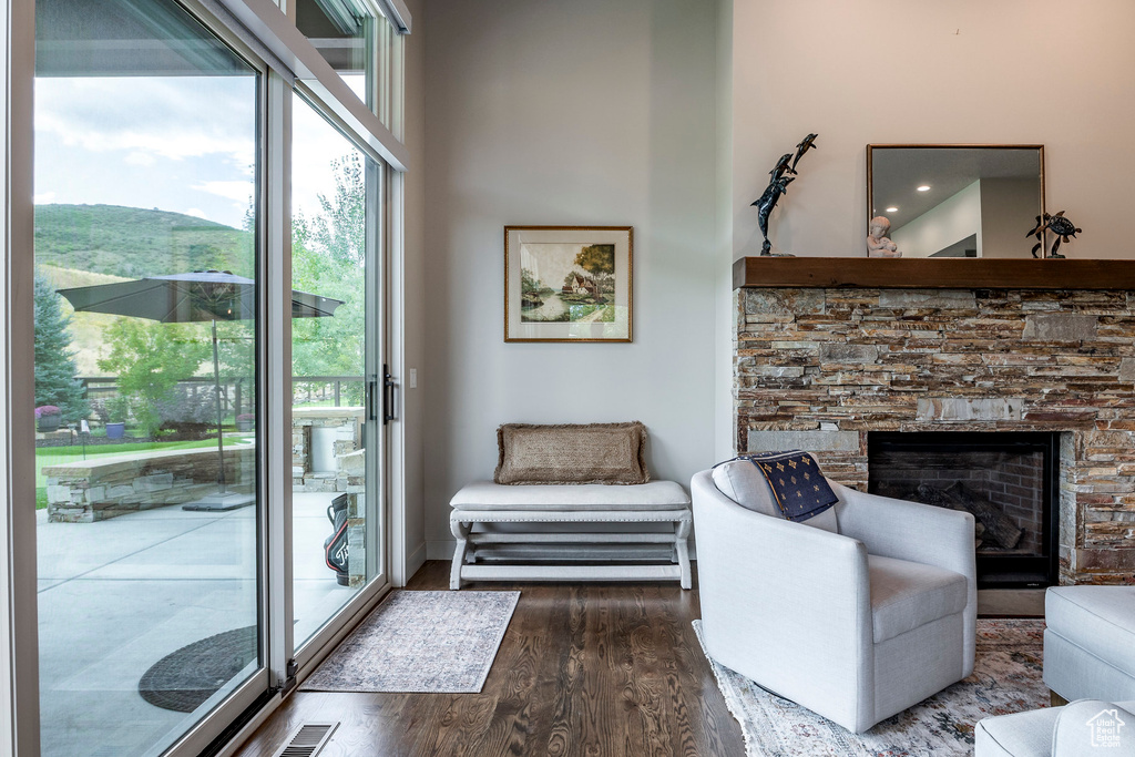 Living area with wood finished floors, plenty of natural light, a high ceiling, and a stone fireplace