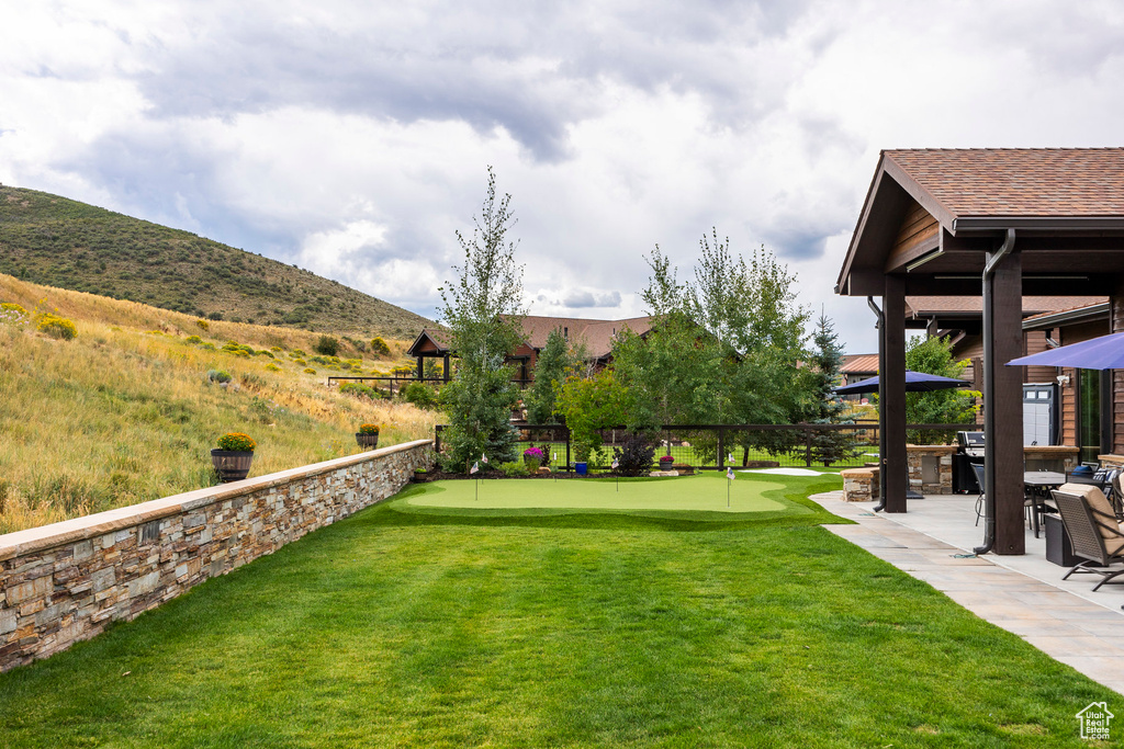 View of grassy yard with a putting green, a patio area, a mountain view, and a gazebo