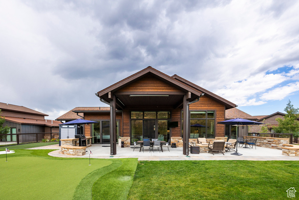 Back of property featuring an area to practice putting, a patio, stone siding, and an outdoor living space with a fire pit