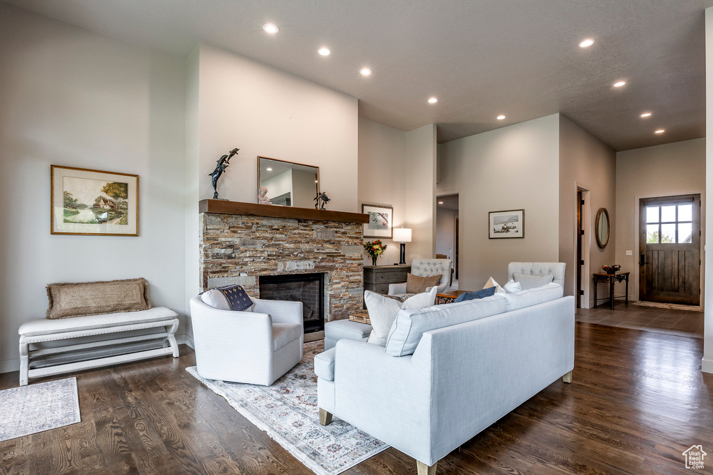 Living room with wood finished floors, recessed lighting, a high ceiling, and a stone fireplace