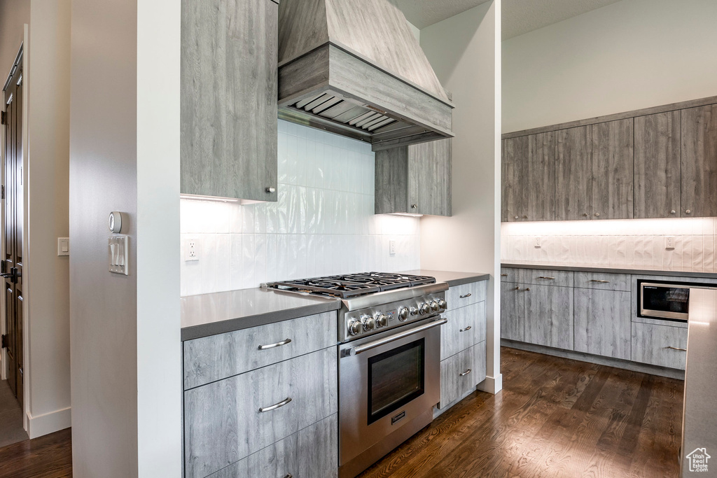 Kitchen featuring high end stove, custom exhaust hood, backsplash, modern cabinets, and dark wood-style flooring