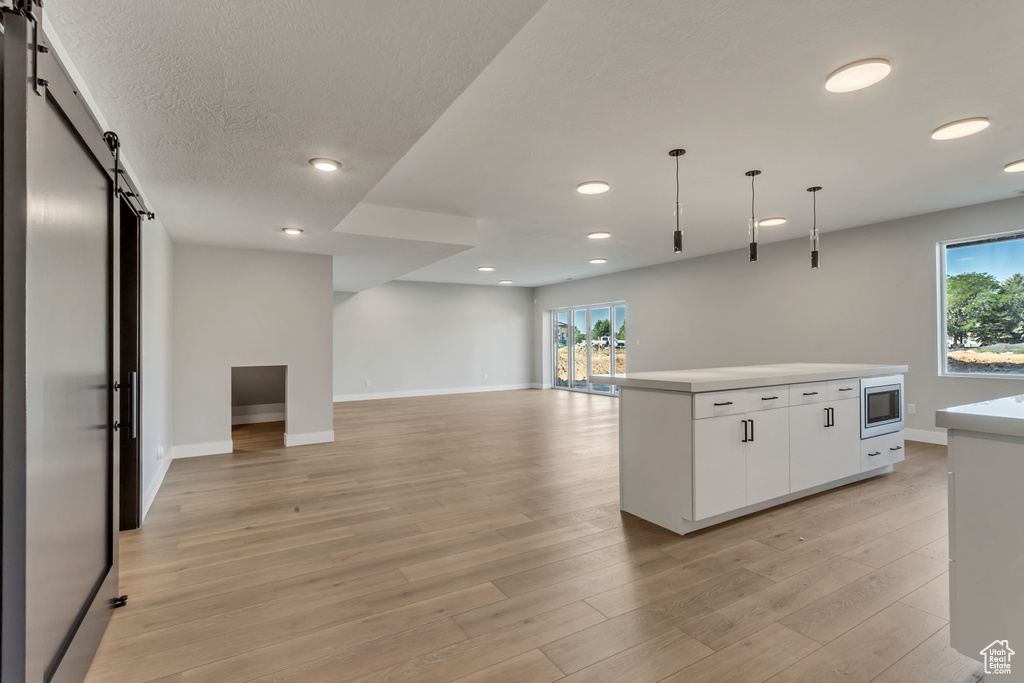 Kitchen with a wealth of natural light, a barn door, stainless steel microwave, and white cabinets