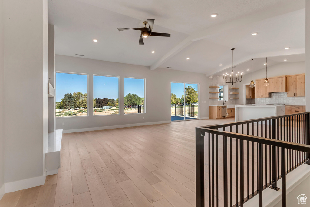 Interior space featuring ceiling fan with notable chandelier, lofted ceiling with beams, and light hardwood / wood-style flooring