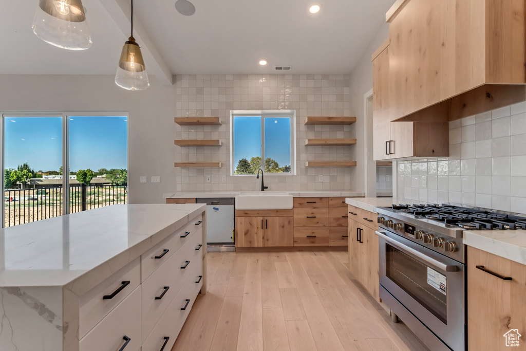 Kitchen featuring decorative light fixtures, appliances with stainless steel finishes, sink, light stone counters, and light wood-type flooring