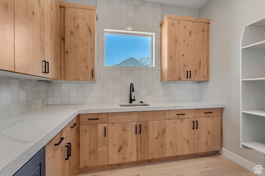 Kitchen with light wood-type flooring, light stone countertops, sink, light brown cabinets, and tasteful backsplash