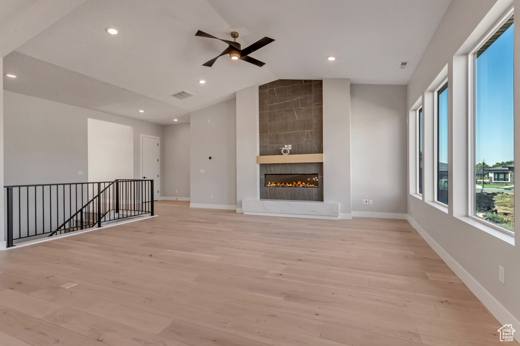 Unfurnished living room with a tile fireplace, light hardwood / wood-style flooring, built in features, lofted ceiling, and ceiling fan