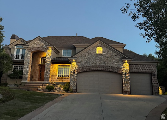 French country inspired facade featuring stone siding, concrete driveway, an attached garage, and a standing seam roof