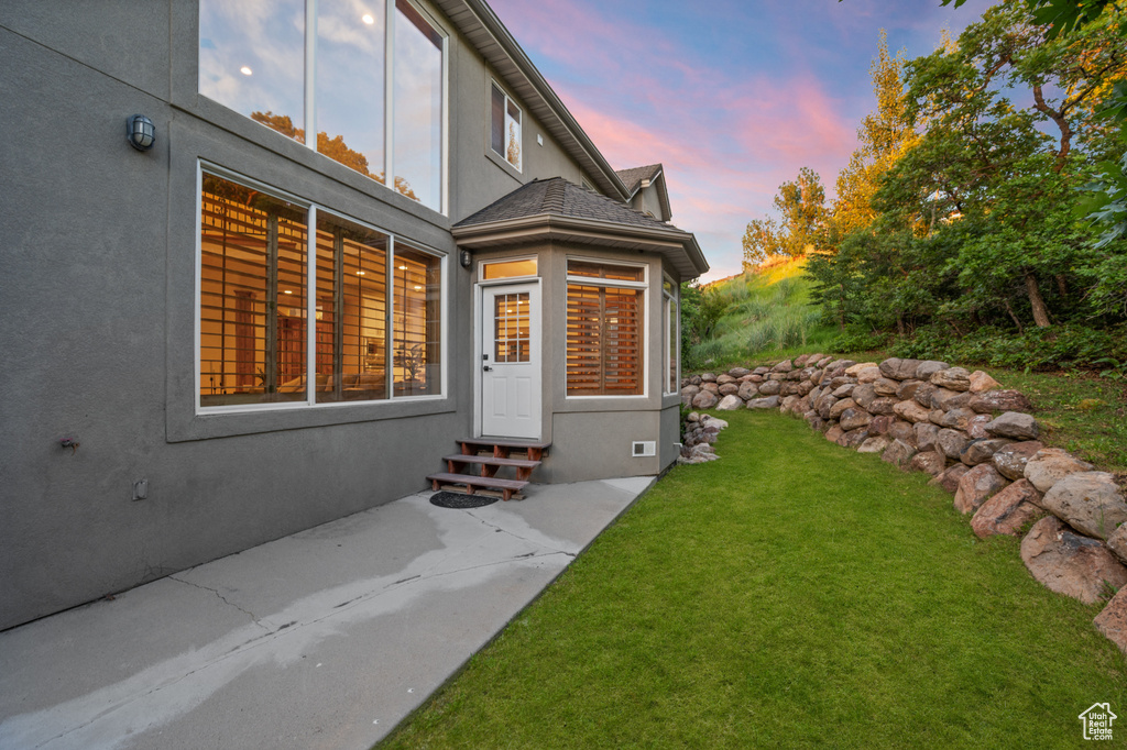 Exterior entry at dusk featuring a lawn and stucco siding