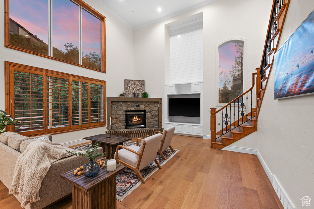 Living area featuring crown molding, a high ceiling, light wood-style floors, a fireplace, and stairway