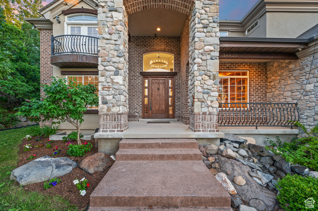 Doorway to property featuring brick siding, a balcony, and covered porch