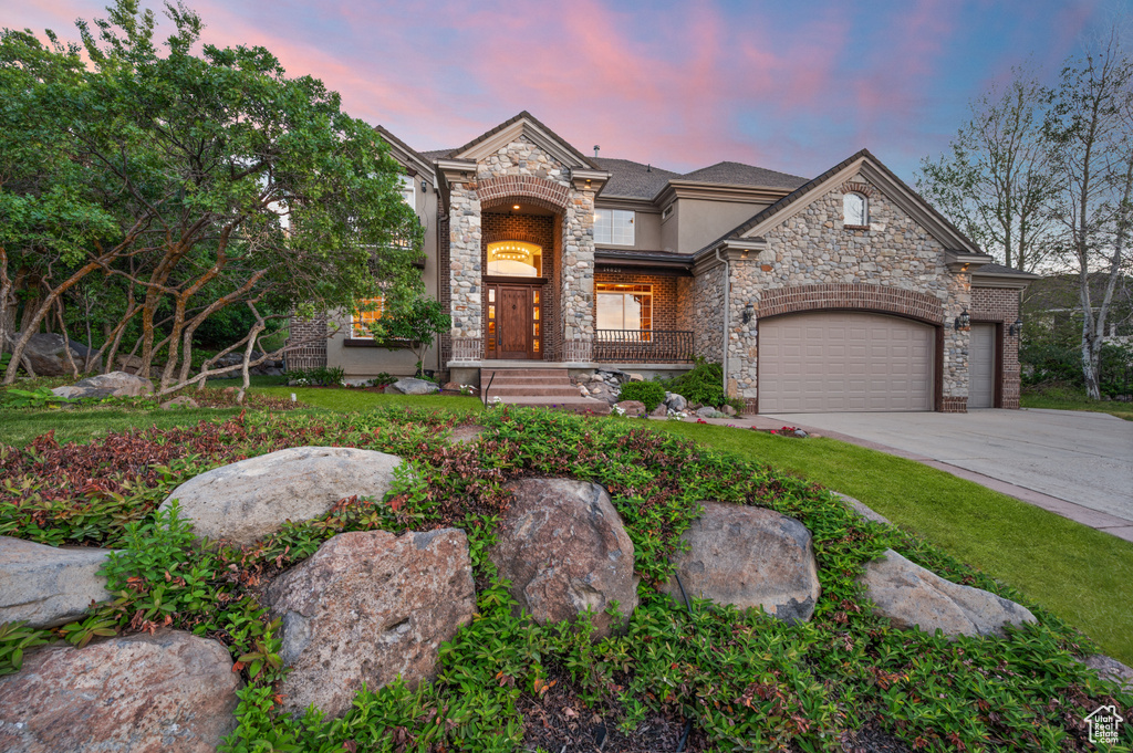 View of front of property with stone siding, an attached garage, concrete driveway, stucco siding, and a porch