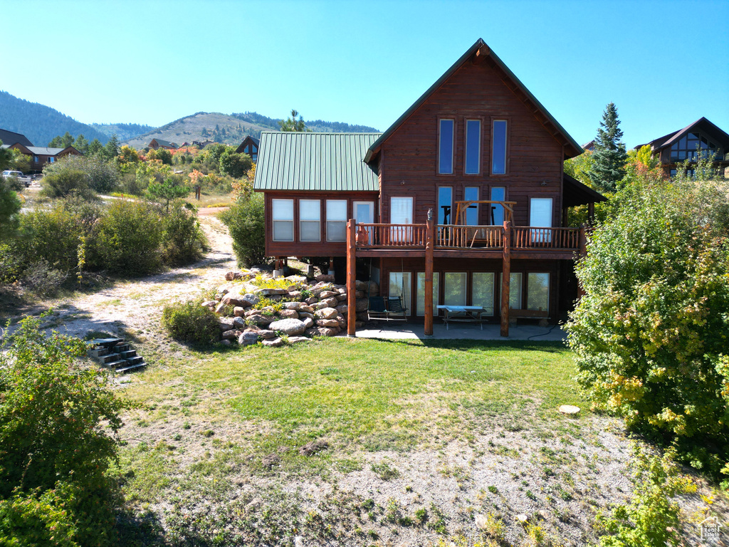 Back of house with a lawn, a patio, and a deck with mountain view