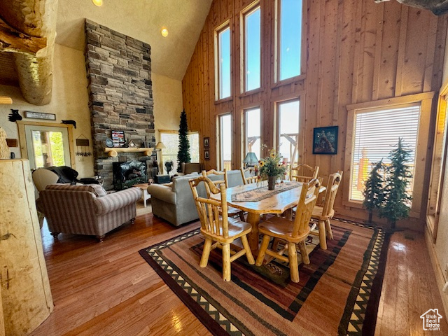 Dining space with hardwood / wood-style flooring, high vaulted ceiling, wooden walls, and a stone fireplace