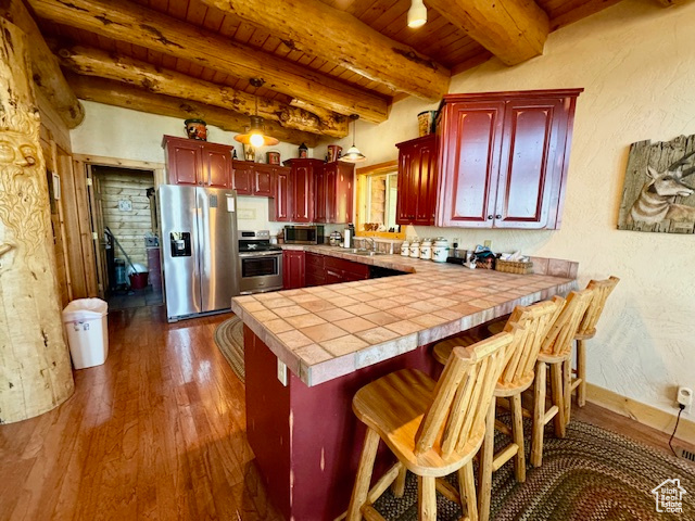 Kitchen with appliances with stainless steel finishes, dark hardwood / wood-style floors, kitchen peninsula, pendant lighting, and a breakfast bar