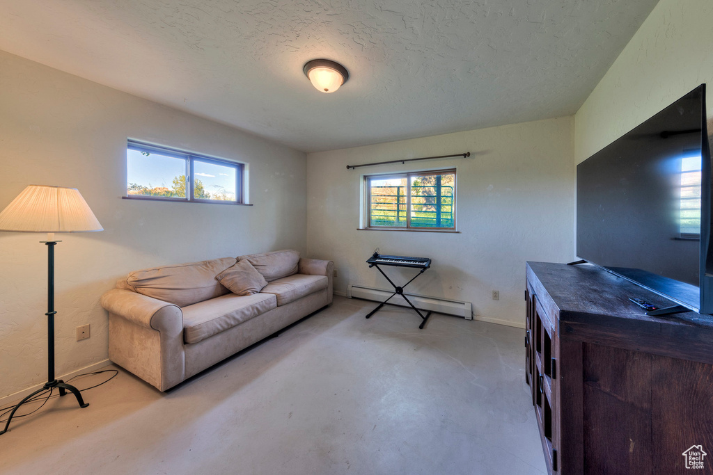 Living area with a baseboard radiator, concrete flooring, a textured ceiling, and baseboards
